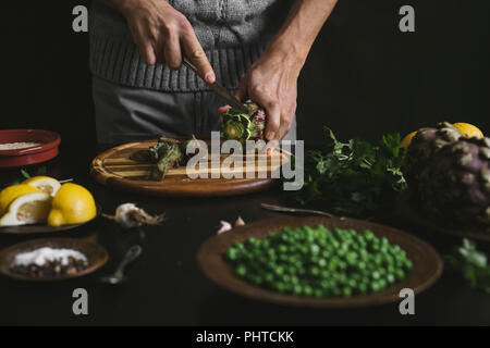 Ein Mann bereitet das Mittagessen mit Artischocken und Erbsen Stockfoto