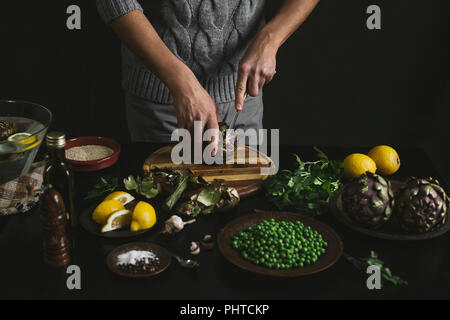 Ein Mann bereitet das Mittagessen mit Artischocken und Erbsen Stockfoto