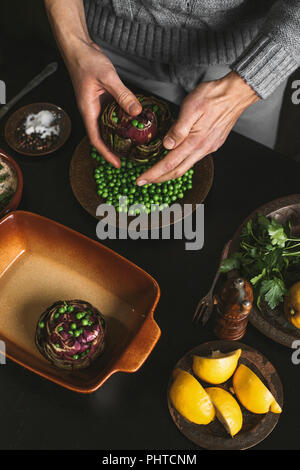 Ein Mann bereitet das Mittagessen mit Artischocken und Erbsen Stockfoto