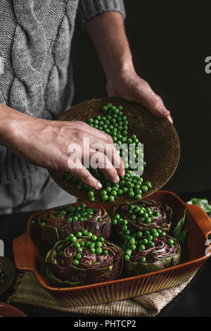 Ein Mann bereitet das Mittagessen mit Artischocken und Erbsen Stockfoto