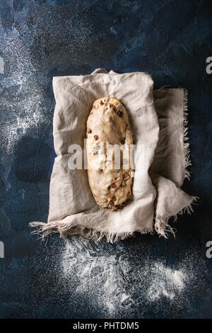 Christmas Cake, traditionelle deutsche Festliches backen. Vollkorn Teig stollen Vorbereitung auf Leinen Serviette über Dunkelblau Textur Hintergrund. Ansicht von oben, s Stockfoto