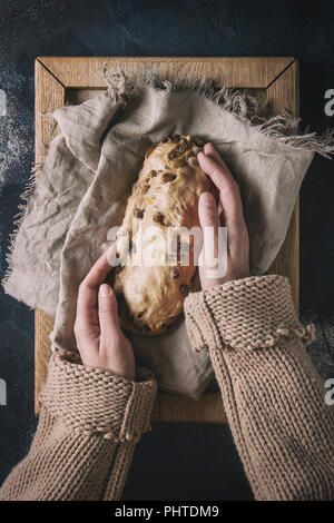 Weihnachtskuchen. Weibliche Hände machen die traditionelle deutsche Festliches backen. Vollkorn Teig stollen Vorbereitung auf Leinen Serviette über Dunkelblau Textur hinterg Stockfoto