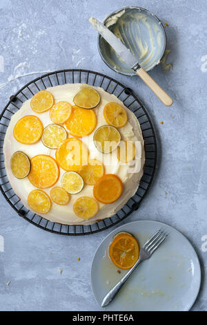 Eine Runde hausgemachte orange Kuchen mit Butter und Puderzucker mit kandierten Zitronen, Limetten und orangen Scheiben eingerichtet. Stockfoto