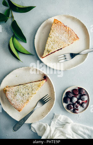 Cherry pie Schichten serviert auf zwei weiße Platten mit Gabeln auf der Seite auf grauem Hintergrund aus Sicht von oben fotografiert. Grüne Blätter und Kirschen entstaubt wi Stockfoto