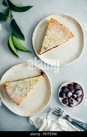 Cherry pie Schichten serviert auf zwei weiße Platten auf grauem Hintergrund aus Sicht von oben fotografiert. Grüne Blätter, Gabeln und Kirschen mit Puderzucker bestäubt Suga Stockfoto