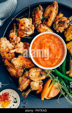 Gegrillte Chicken Wings sind auf einer schwarzen Fach von gegrilltem Mais, Paprika, frischem Thymian, Pfirsich Schichten und einer Schüssel mit Zucker frei bbq sa begleitet werden, Stockfoto