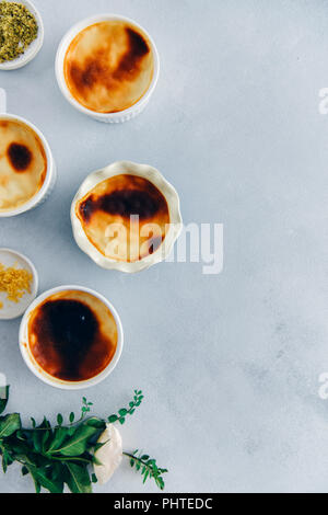 Gebackener Reis Pudding in Förmchen fotografiert auf einem grauen Hintergrund von oben ansehen. Zitronenschale und Boden Pistazien in kleinen Schüsseln und eine weiße Rose mit g Stockfoto