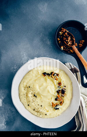 Cheesy Kartoffelpüree mit gerösteten Walnüssen und schwarzer Pfeffer in eine weiße Keramik Schüssel auf einem dunklen Hintergrund aus Sicht von oben fotografiert. Stockfoto