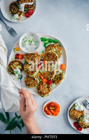 Hand verbreiten Gurken Joghurt dip auf Zucchini Krapfen auf einem weißen Keramik Platte von der Ansicht von oben fotografiert. Stockfoto