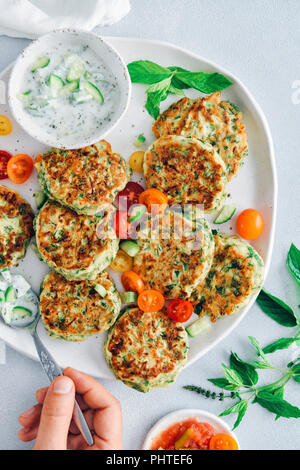 Hand verbreiten Gurken Joghurt dip auf Zucchini Krapfen auf einem weißen Keramik Platte von der Ansicht von oben fotografiert. Stockfoto