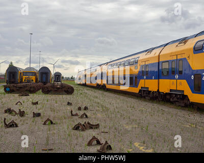 Dual Deck Zug Passagiere warten auf Kutschen zur Verfügung Neben Reihen von Zug Motor Drehgestelle und Bremse Teile auf dem Boden verstreut. Holland. Stockfoto