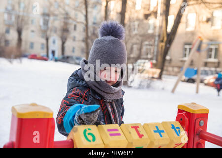 Ernsthafte junge 4 Jahre im Winter auf dem Spielplatz spielen Würfel mit Zahlen Stockfoto