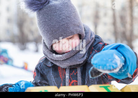 Ernsthafte junge 4 Jahre im Winter auf dem Spielplatz spielen Würfel mit Zahlen Stockfoto