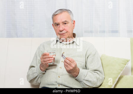 Enttäuscht älterer Mann sitzt auf dem Sofa und der Einnahme von Tabletten. Stockfoto