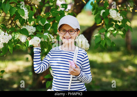 Kleines Mädchen Kind auf einem Hintergrund von White Lilac Bush. Stockfoto