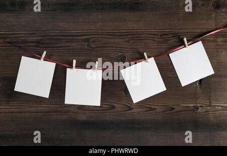 Vier leere Fotopapier an Seil mit Wäscheklammern auf Holz- Hintergrund. Stockfoto