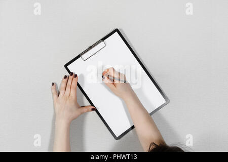 Frau schreibt auf leeres weißes Blatt Papier. Zwischenablage in weibliche Hände. Flach. Stockfoto