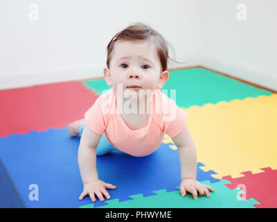 Portrait von cute adorable Kaukasischen smiling baby junge Mädchen liegt auf Fußboden im Kinderzimmer in der Kamera suchen, natürliche Fenster Licht, Lifestyle Stockfoto