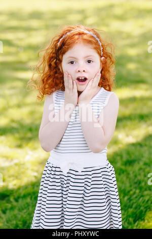 Portrait von cute adorable überrascht wenig Rothaarige kaukasische Mädchen in gestreiften Kleid in Park draußen spielen Schreien schreien vor Angst, glücklich Stockfoto