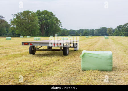 Trailer im Gras Feld mit Plastifizierten Heuballen Stockfoto