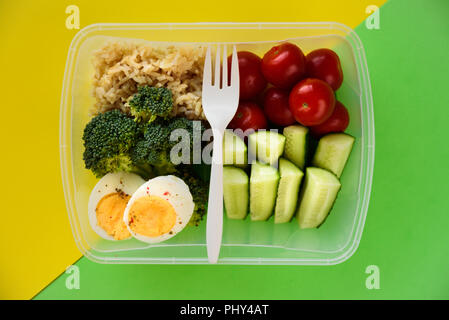 Lunch Box mit gesunden Lebensmitteln. Reis, Brokkoli, Tomaten, Gurken, Eier, Apple und Wasser. Auf gelben und grünen Hintergrund Stockfoto