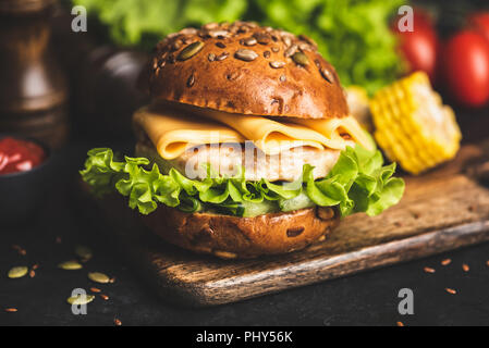 Huhn Cheeseburger auf Vollkorn Brötchen mit Salat und gegrilltem Mais auf Holz serviert. Detailansicht Stockfoto