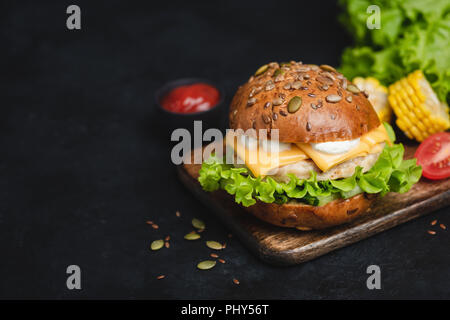 Classic Cheeseburger auf dunklem Hintergrund mit Sauce, Salat, Tomaten und Käse. Kopieren Sie Platz für Text Stockfoto