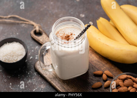 Banane protein Smoothie oder Milchshake mit Zimt und Kokosnuss in ein trinkendes Glas mit staw. Detailansicht, selektiver Fokus Stockfoto