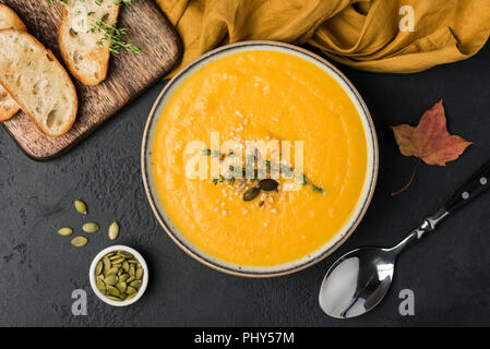 Kürbis creme Suppe Schüssel auf schwarzen Hintergrund. Ansicht von oben. Herbst Hausmannskost, vegetarische gesunde Ernährung Stockfoto