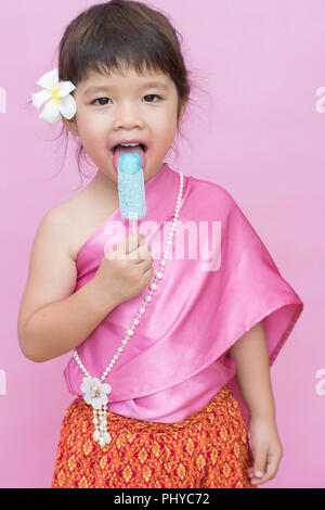 Portrait lächelnde Mädchen in thailändischen traditionellen antiken Kleid essen Popsicle auf rosa Hintergrund isoliert. Stockfoto
