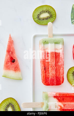 Appetitlich Zusammensetzung von Eis am Stiel auf einem Stick und saftige Stücke Wassermelone und Kiwi auf grauem Marmor Hintergrund mit kopieren. Flach Stockfoto