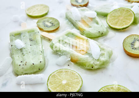 Frozen Smoothies mit einem Stück mango präsentiert auf grauem Hintergrund mit Stücken Eis, Kiwi und Kalk. Gesund Sommer Nachtisch. Flach Stockfoto