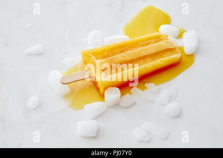 Orange Frucht Eis auf einem Stick mit Scheiben von Eis auf einem grauem Marmor Hintergrund mit Platz für Text. Flach Stockfoto