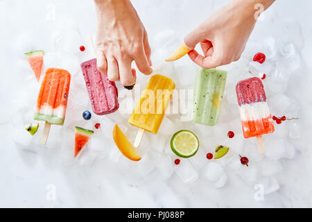 Die Hände der Frau, dekorieren Sie das Eis auf einem Stick mit Bits von saftigen Früchte. Sommer Nachtisch. Flach Stockfoto