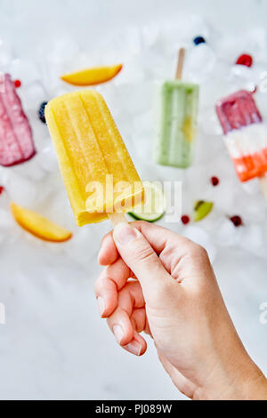 Gefrorene Beere Smoothies auf einem Stick mit Früchten. Die Hand des Mädchens nimmt einen Smoothie auf einem Stick von Eiswürfeln. Flach Stockfoto