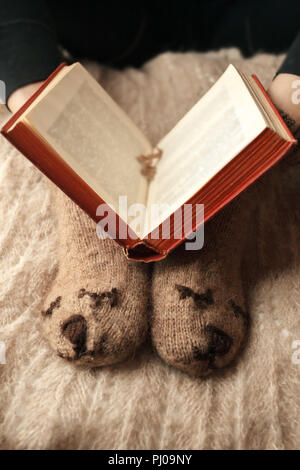 Weiche Foto von Frau Beine in süßen lustige Bär braun Socken auf dem Bett mit alten Buch, monochromes Konzept, Zeit zum Lesen, Herbst und Winter Stockfoto
