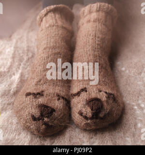 Gemütliche Winter Herbst Herbst Lifestyle: Frau feets Beine in warmen süssen Bär Socken. Retro, Tonisierung, beige Monochrom, hipster Still Life Stockfoto