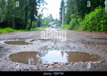 Bohrungen und Schlagloch auf eine Landstraße nach Regen im Frühjahr Stockfoto