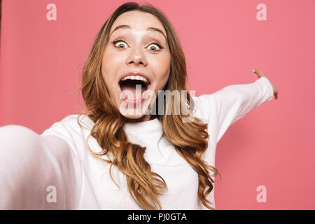 Portrait von eine fröhliche junge Frau unter selfie mit ausgestreckter Hand über rosa Hintergrund isoliert Stockfoto