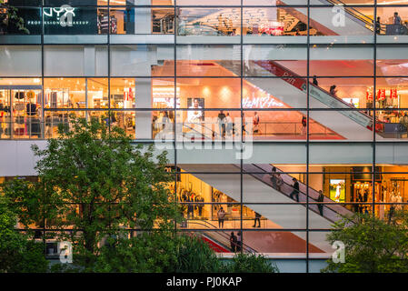 Leben Der EmQuartier Shopping Mall (Bangkok, Thailand) durch das Glas in der Nacht, und Bäume, die auf den Garten im Innenhof in der Abenddämmerung. Stockfoto