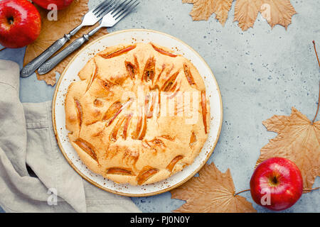 Leckere hausgemachte Saison Apple Pie von Ahorn verwelkten Blättern und roten Äpfeln umgeben. Herbst Bäckerei, gemütliche Feiertage. Stockfoto