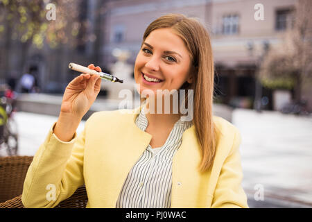 Schöne junge Frau, die elektronische Zigarette im Café. Stockfoto