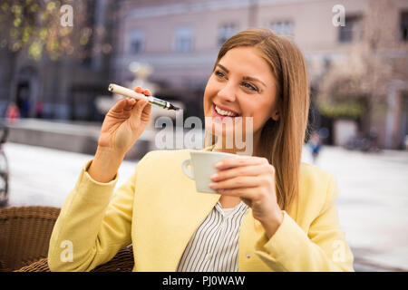 Schöne junge Frau, die elektronische Zigarette und trinken Kaffee im Café. Stockfoto