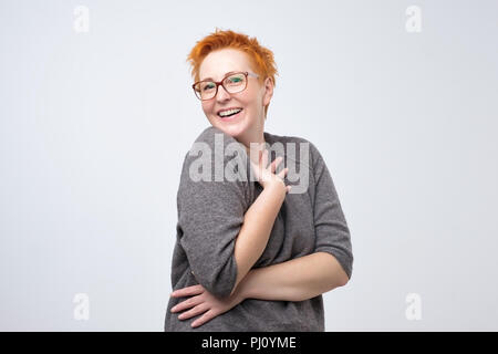 Ziemlich kaukasischen reife Frau mit kurzen roten Frisur in einfachen pulover ist schüchtern ein Kompliment zu hören. Stockfoto