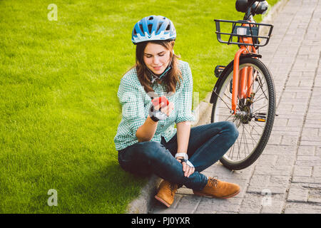 Mensch und Stadt rollenden Fahrrad, umweltfreundliche Verkehrsmittel. Schönen jungen kaukasischen Arbeiterin sitzen ruht auf dem Gras verwendet eine rote mobil Stockfoto