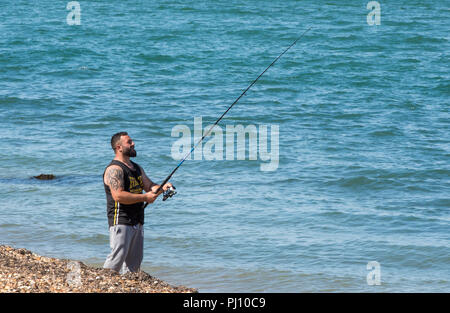 Ein Mann stand am Strand in der Nähe des Meeres mit einer Angelrute. Meeresangeln oder Angler. Stockfoto