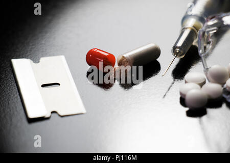 Droge-utensilienien auf schwarzem Hintergrund. Pillen, Nadeln, Rasierklingen. Narkotische Objekte Drogenmissbrauch und Drogenabhängigkeit. Stockfoto