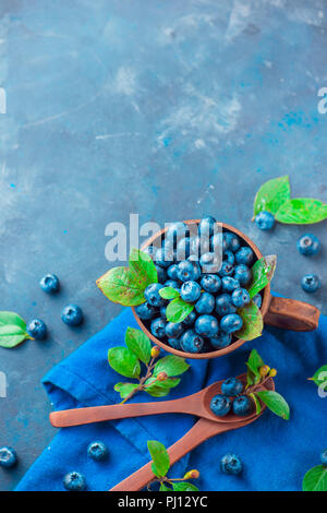 Sommer Beeren flach. Heidelbeeren im keramiktasse mit holzlöffel von oben. Neutrale Farben, Blau und Grau Palette, kopieren Raum Stockfoto