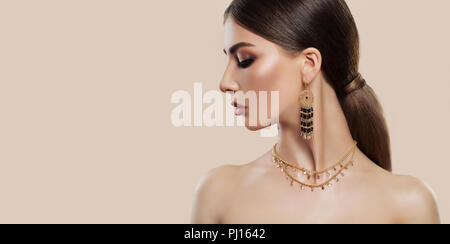 Elegante Frau mit Modeschmuck auf rosa Hintergrund. Gold Schmuck für die Frau, die Halskette und Ohrringe mit schwarzen Edelsteinen. Schönheit und Zubehör. Stockfoto