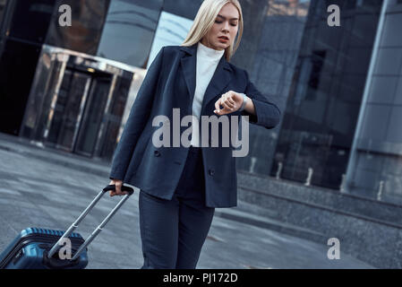 Frau mit Blick auf ihr Handgelenk beobachten, während die Kontrolle der Zeit gehen auf die Stadt Hintergrund Stockfoto